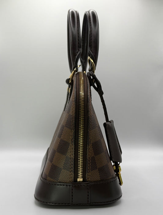 Louis Vuitton Alma BB Damier Ebène, three-quarter view highlighting dual rolled leather handles and zip closure