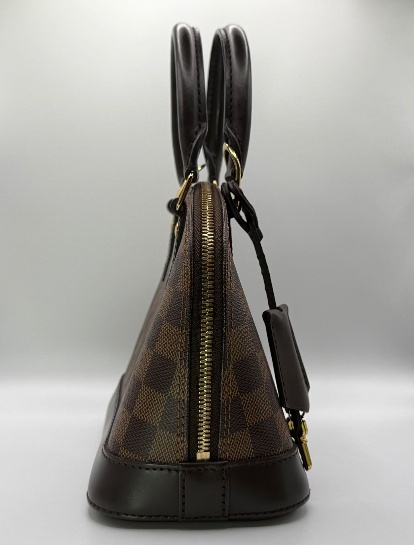 Louis Vuitton Alma BB Damier Ebène, three-quarter view highlighting dual rolled leather handles and zip closure