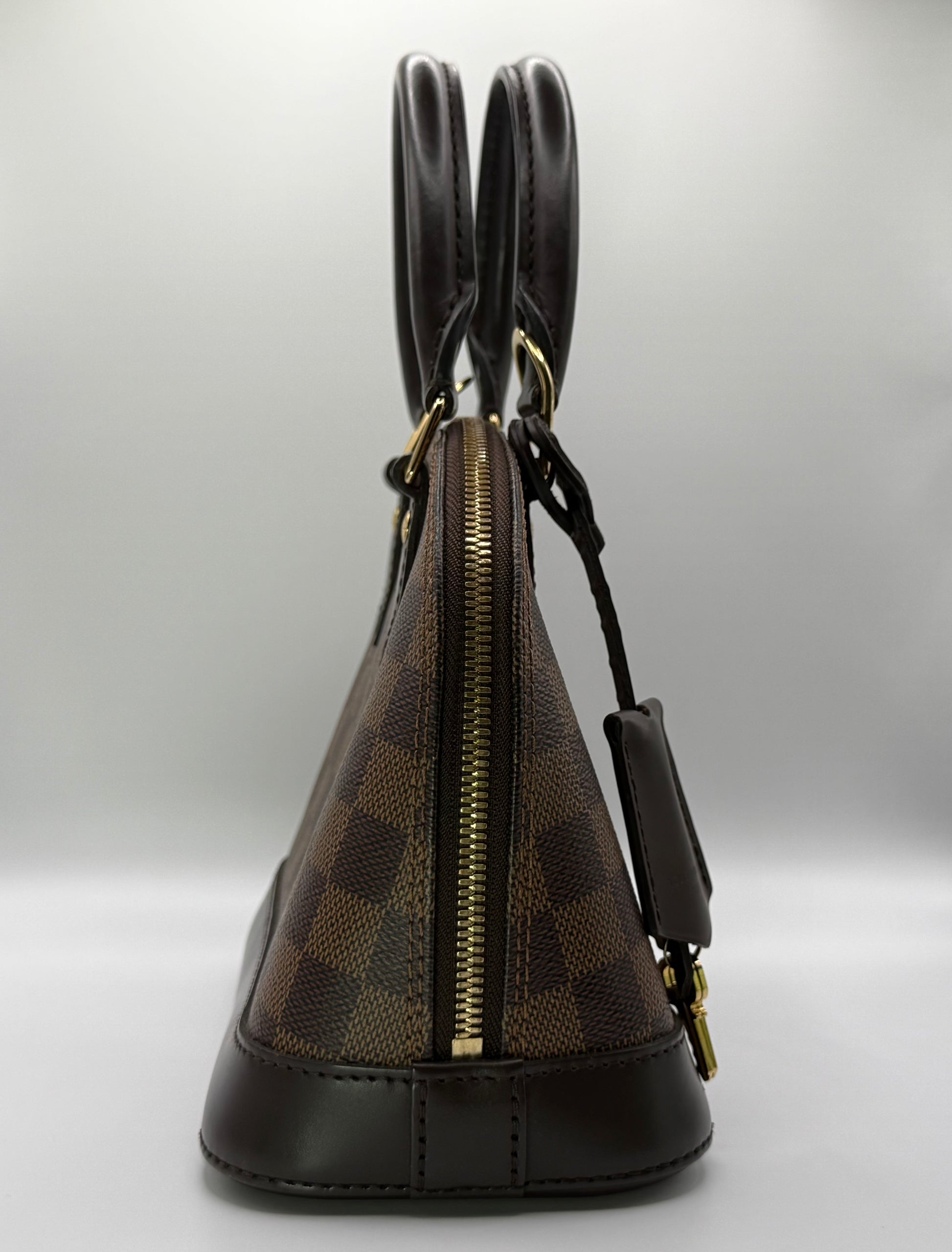 Louis Vuitton Alma BB Damier Ebène, three-quarter view highlighting dual rolled leather handles and zip closure