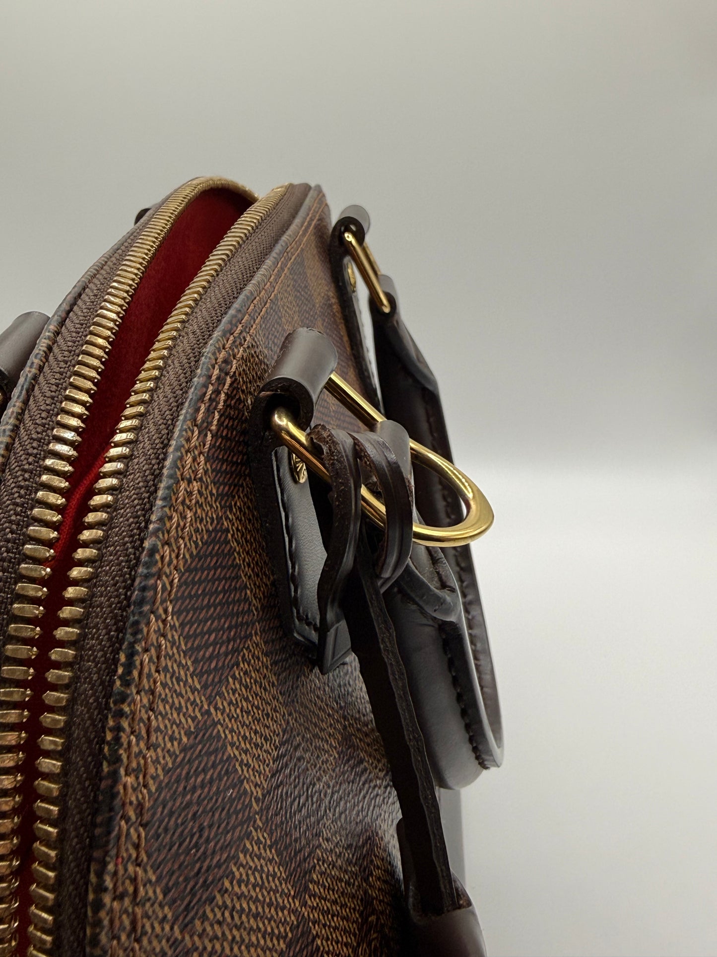 Louis Vuitton Alma BB Damier Ebène, close-up of gold-tone LV padlock and key with leather tab