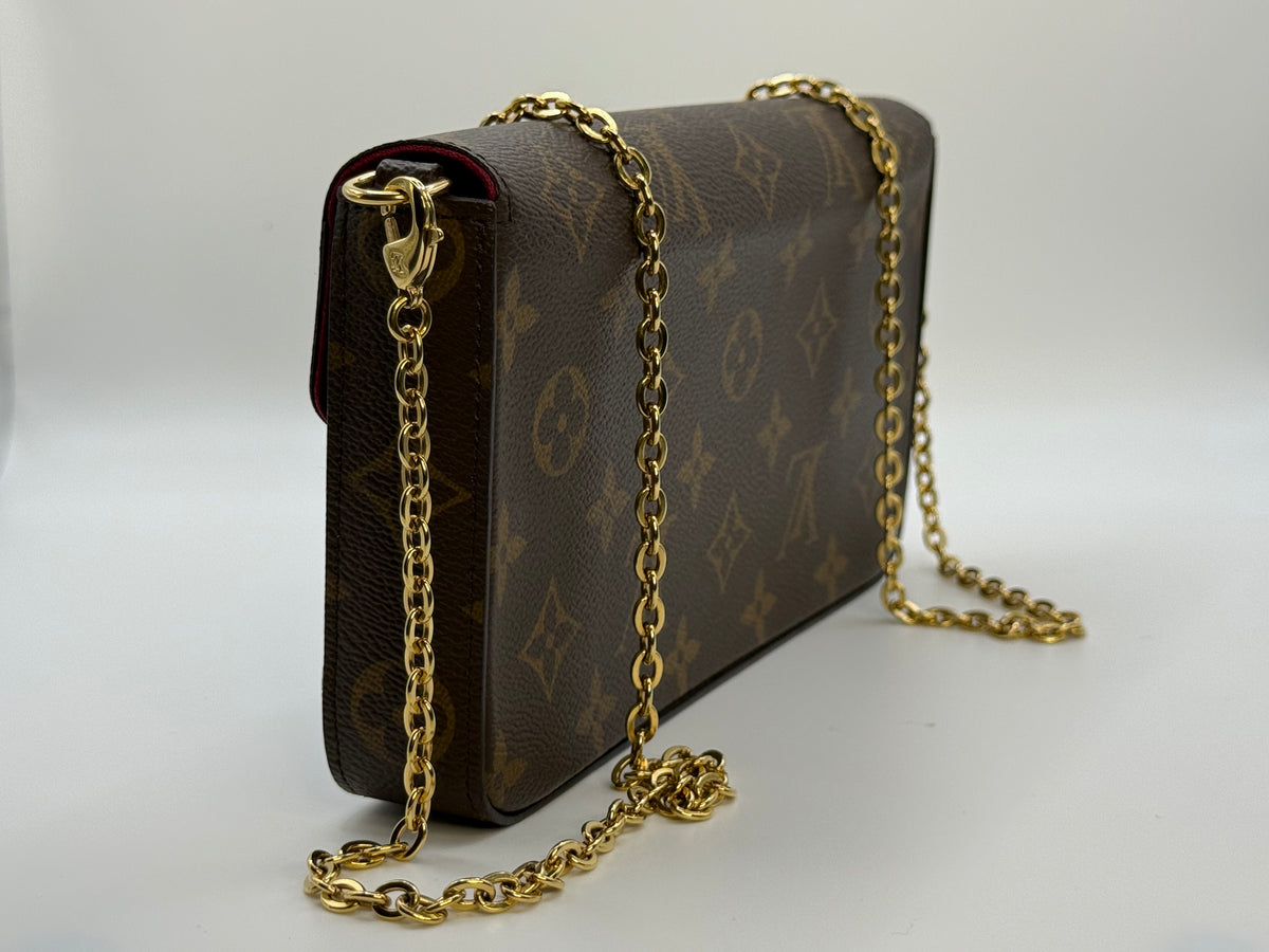 Louis Vuitton Félicie Pochette shown at an angle with gold-tone chain strap attached, on white background