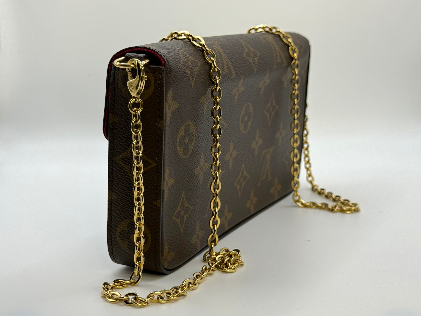 Louis Vuitton Félicie Pochette shown at an angle with gold-tone chain strap attached, on white background