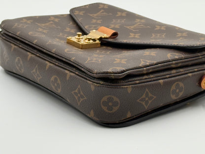 Louis Vuitton Pochette Métis Monogram — close-up of gold S-lock and vachetta tab with honey patina